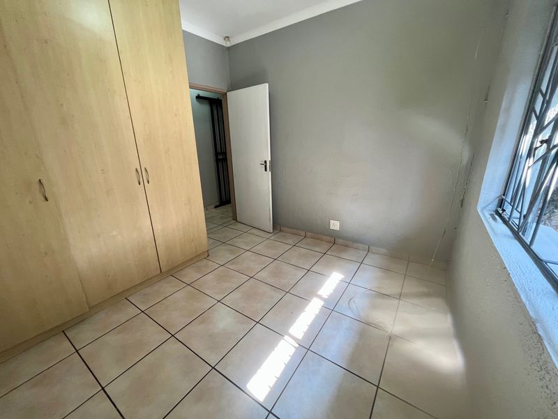 An empty bedroom featuring tiled flooring, a built-in wardrobe, and security bars on the window.