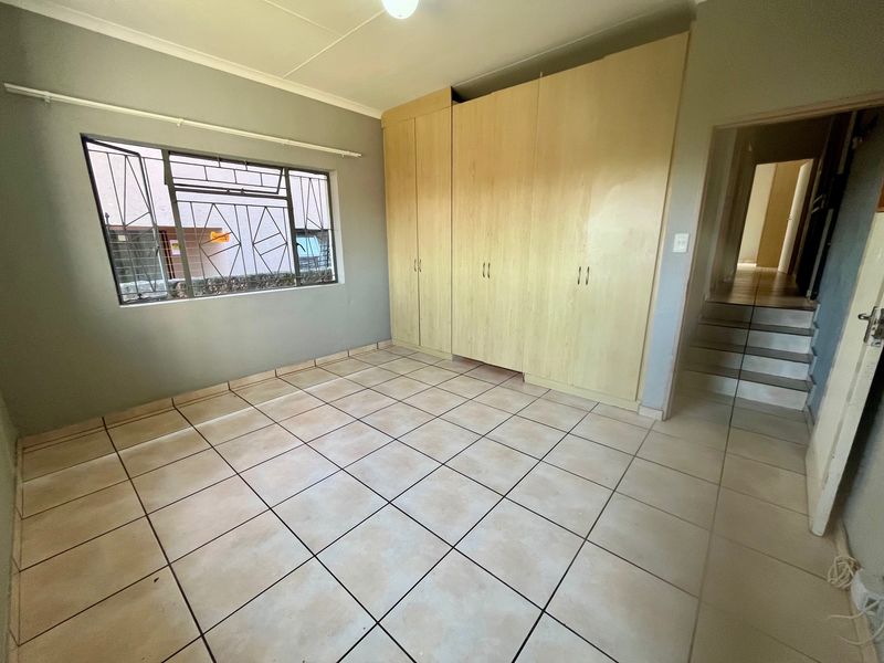 A vacant bedroom featuring built-in cupboards, tiled flooring, and security bars on the window, offering a neutral space ready for personalization.