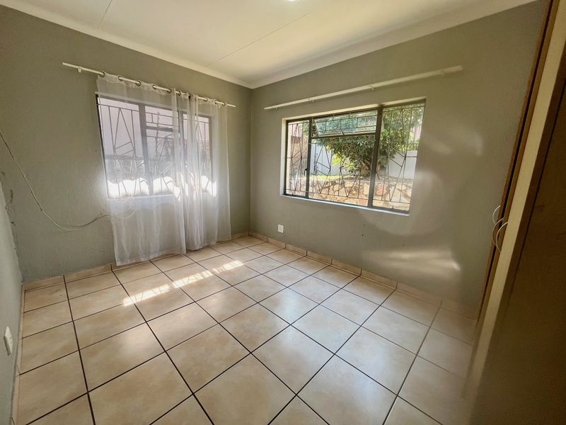 A vacant bedroom featuring neutral tiled flooring, built-in storage, and security bars on the windows, offering a clean canvas for personalization.