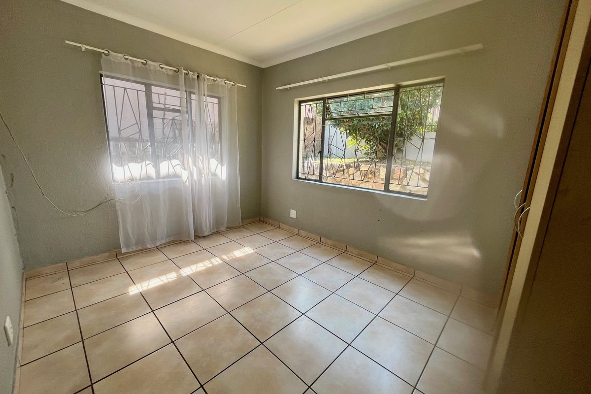 A vacant bedroom featuring neutral tiled flooring, built-in storage, and security bars on the windows, offering a clean canvas for personalization.
