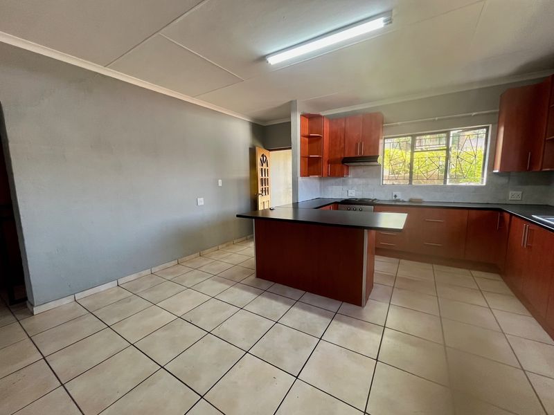 A functional kitchen featuring wooden cabinetry, a central island, dark countertops, and ceramic tile flooring, offering a practical layout for daily use.