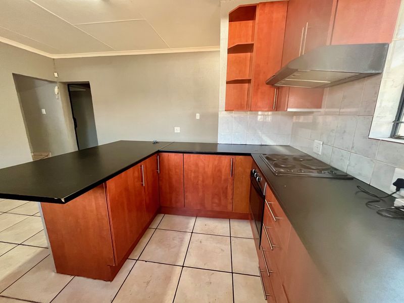 A functional kitchen featuring wood-tone cabinetry, black countertops, built-in oven, electric hob, and tiled flooring, offering a practical layout for daily use.