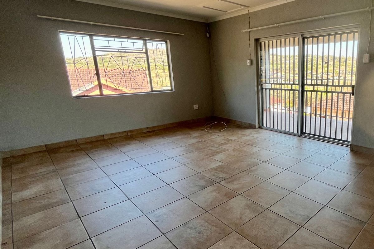 An empty living room featuring tiled flooring, a sliding door with security gate, and a window with security bars, offering a blank canvas for renovation.