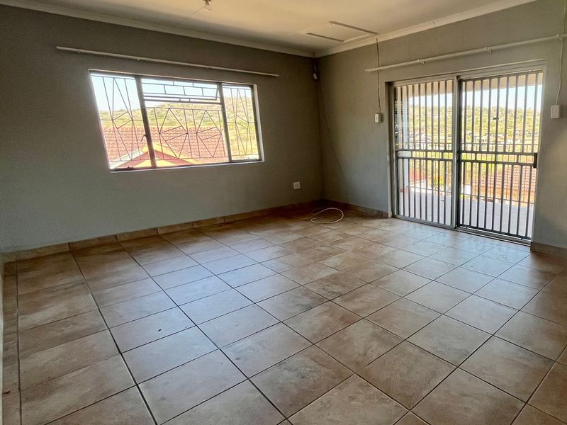 An empty living room featuring tiled flooring, a sliding door with security gate, and a window with security bars, offering a blank canvas for renovation.