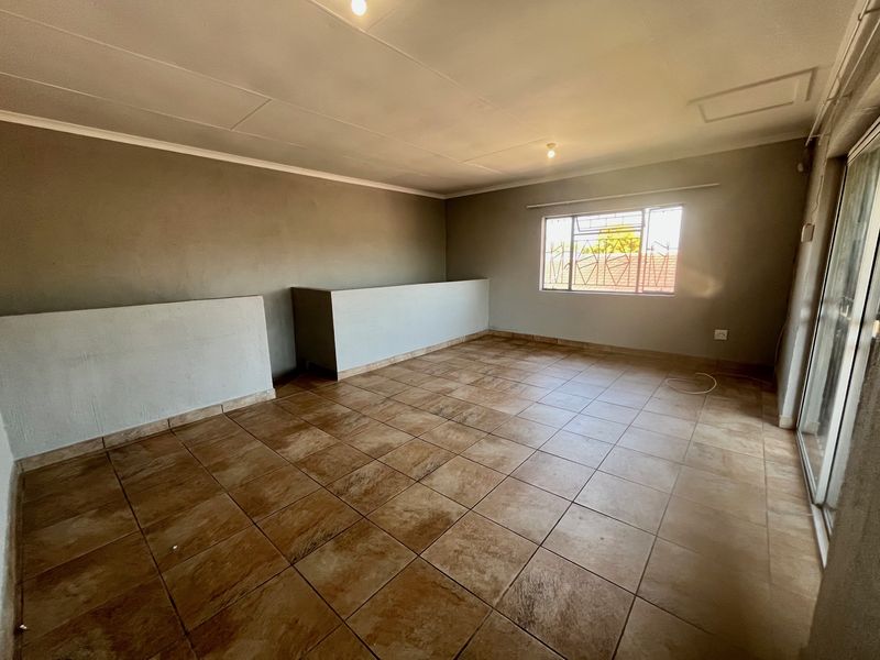An empty, open-plan living area featuring tiled flooring, security bars on the window, and a sliding glass door leading to the exterior.