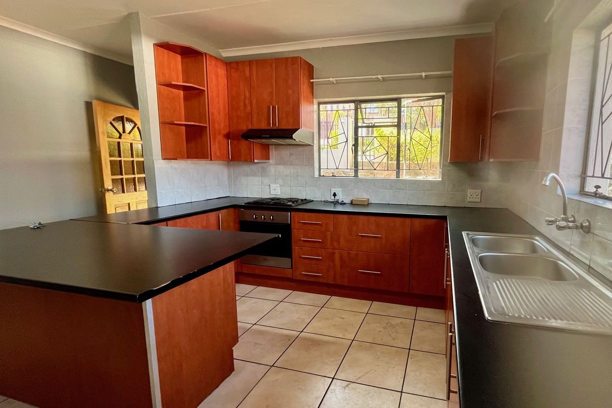 A functional kitchen featuring wooden cabinetry, dark countertops, a built-in oven with gas hob, and tiled flooring.