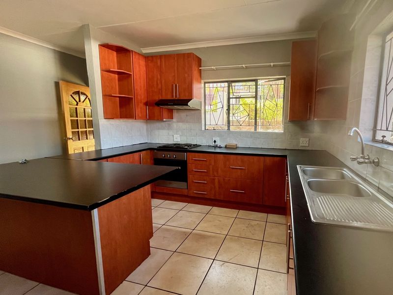 A functional kitchen featuring wooden cabinetry, dark countertops, a built-in oven with gas hob, and tiled flooring.
