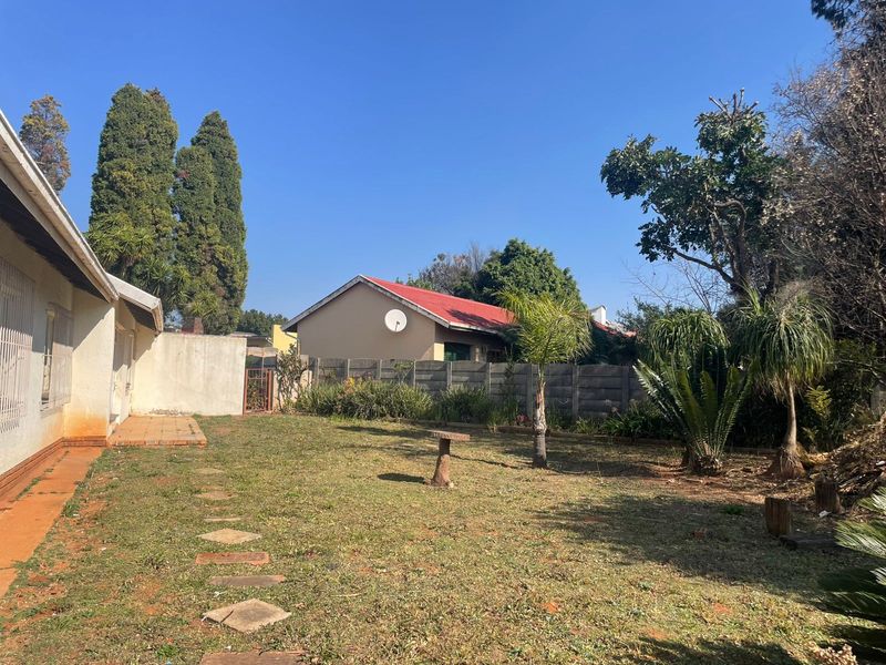 A rear garden view featuring a lawn, paved walkway, and precast concrete boundary wall, showing signs of wear and maintenance needs.