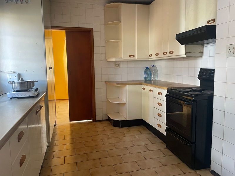 A functional kitchen featuring built-in cabinetry, tiled splashbacks, and a freestanding stove, offering a dated aesthetic ready for modernization.