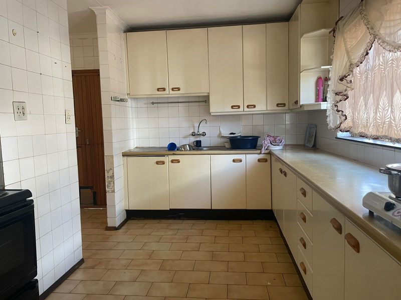 A dated kitchen featuring original built-in cabinetry, laminate countertops, and ceramic wall and floor tiles, offering significant potential for a modern renovation.