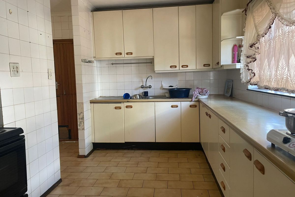 A dated kitchen featuring original built-in cabinetry, laminate countertops, and ceramic wall and floor tiles, offering significant potential for a modern renovation.