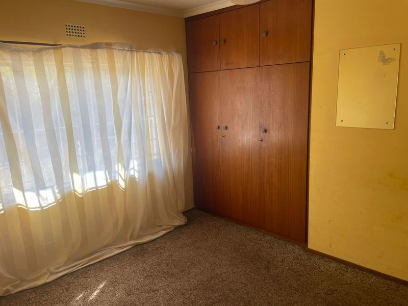 A bedroom featuring built-in wooden wardrobes, carpet flooring, and a ventilation grille, presenting a dated interior in need of cosmetic updates.