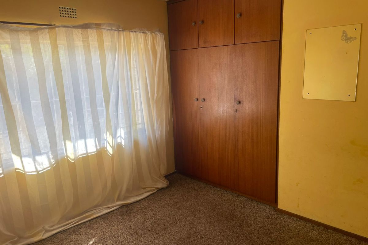 A bedroom featuring built-in wooden wardrobes, carpet flooring, and a ventilation grille, presenting a dated interior in need of cosmetic updates.