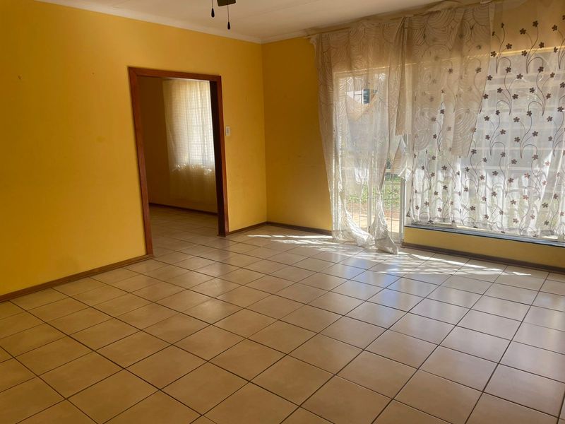 An empty living room featuring ceramic floor tiles, a timber door frame, and a ceiling fan, with access to an adjacent room.