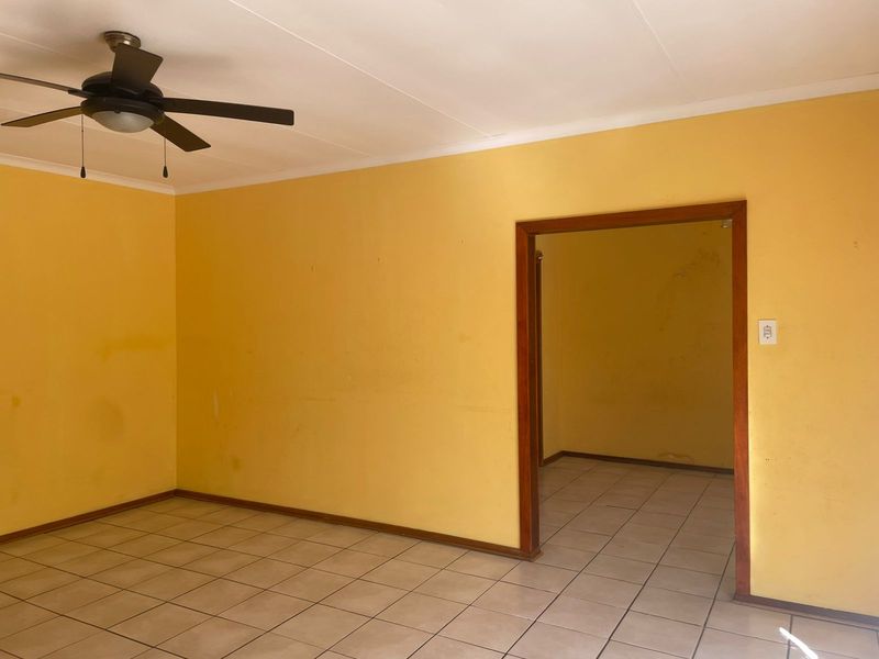 An empty living room featuring ceramic floor tiles, a ceiling fan, and yellow painted walls with visible wear and scuffing.