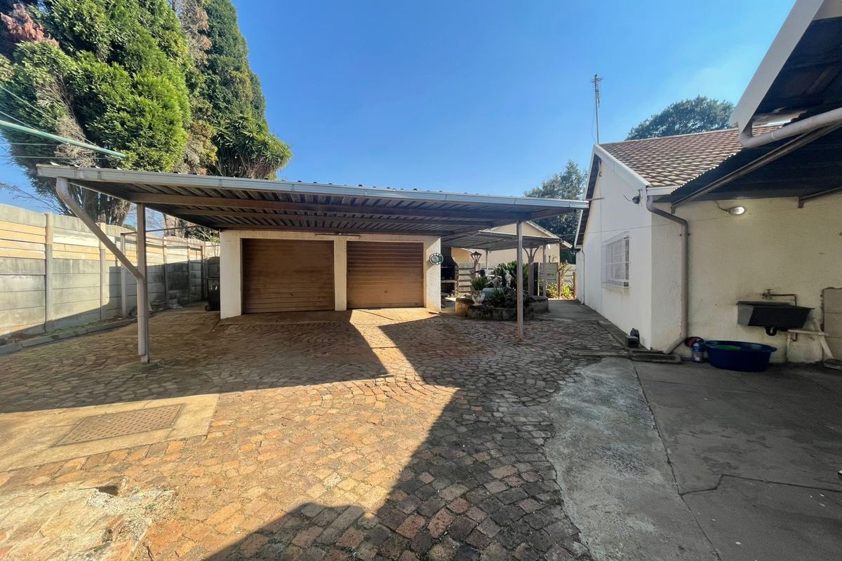 Rear exterior view featuring a double carport, paved driveway, and double garage doors with an adjacent external wash basin.