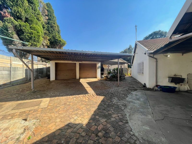 Rear exterior view featuring a double carport, paved driveway, and double garage doors with an adjacent external wash basin.