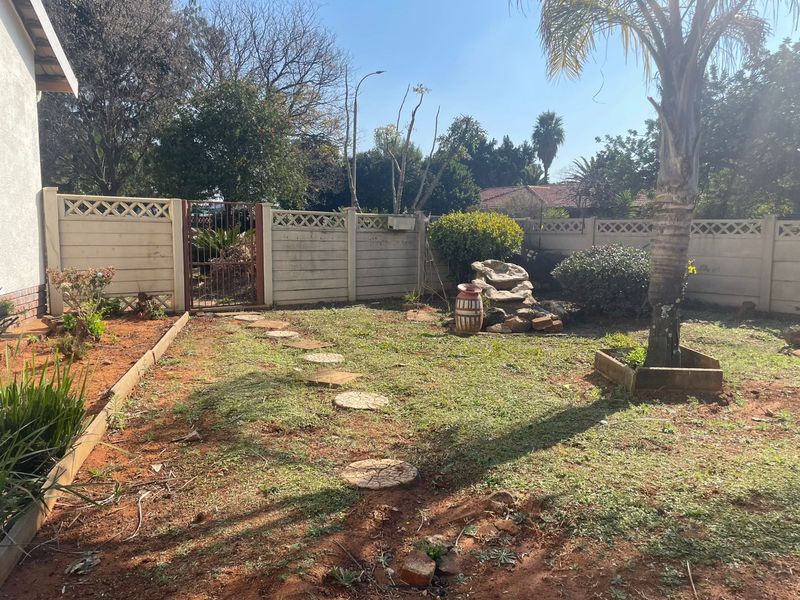 A private garden area featuring a precast concrete boundary wall, a metal access gate, a stone water feature, and established landscaping.