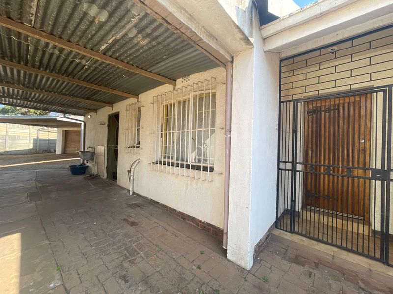 Covered outdoor patio area featuring paved flooring, security gates, and an external sink, providing a functional transition space to the home entrance.