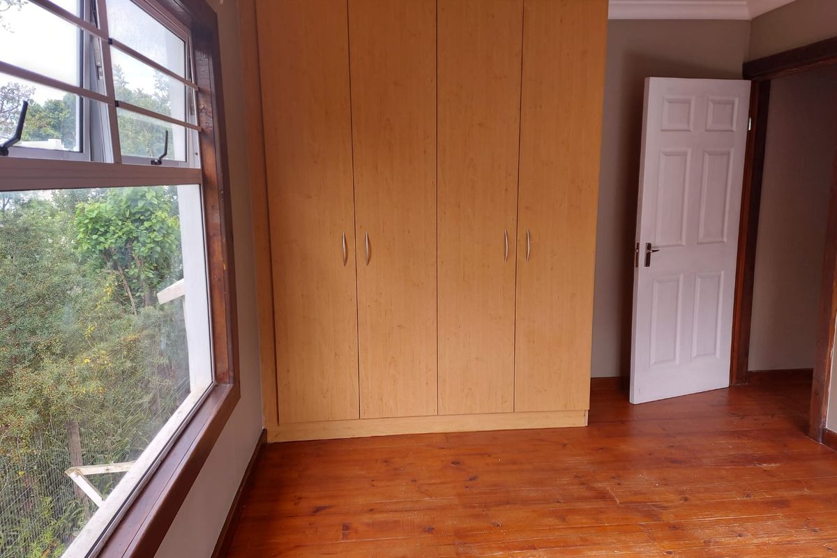 A bedroom featuring timber flooring, built-in cupboards, and a large window with an exterior view.