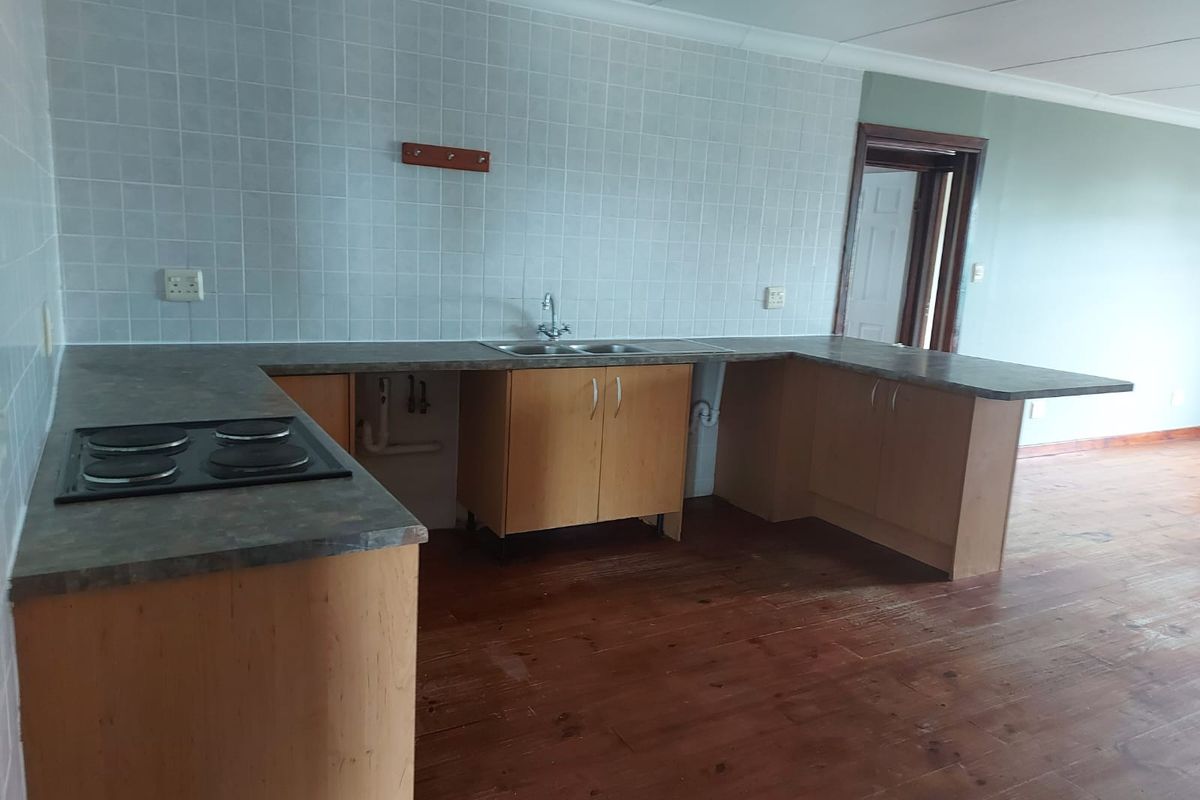 An open-plan kitchen area featuring timber cabinetry, laminate countertops, a built-in electric hob, and a double bowl sink with tiled splashback.