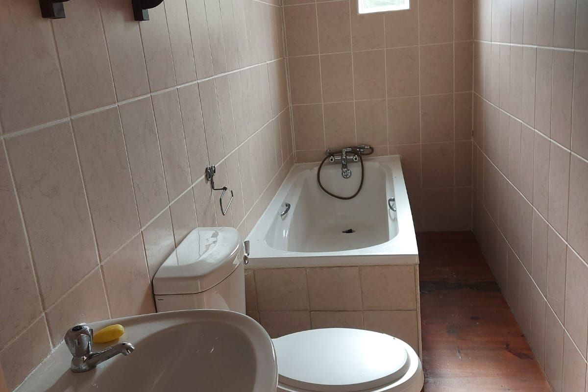 A functional bathroom featuring a bathtub, pedestal basin, and toilet, finished with tiled walls and wooden flooring.