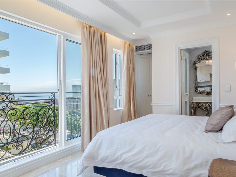 Elegant bedroom featuring marble flooring, crown molding, and a private balcony with wrought iron railings, offering seamless access to an en-suite bathroom.