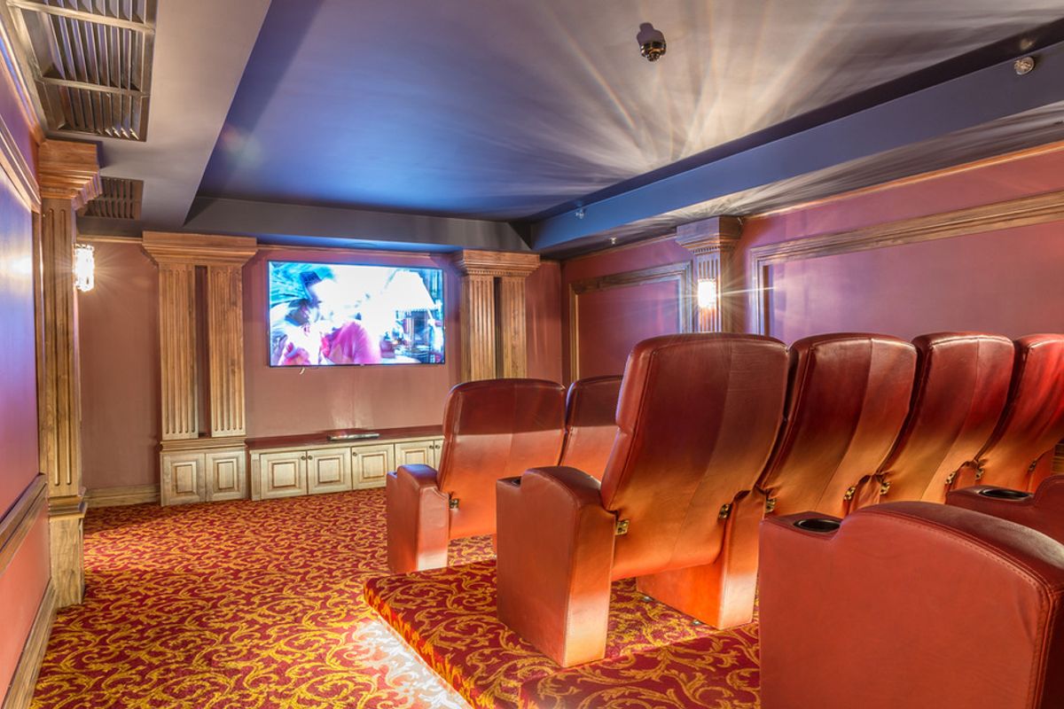 A dedicated home cinema room featuring tiered seating, decorative wall columns, built-in cabinetry, and integrated lighting.