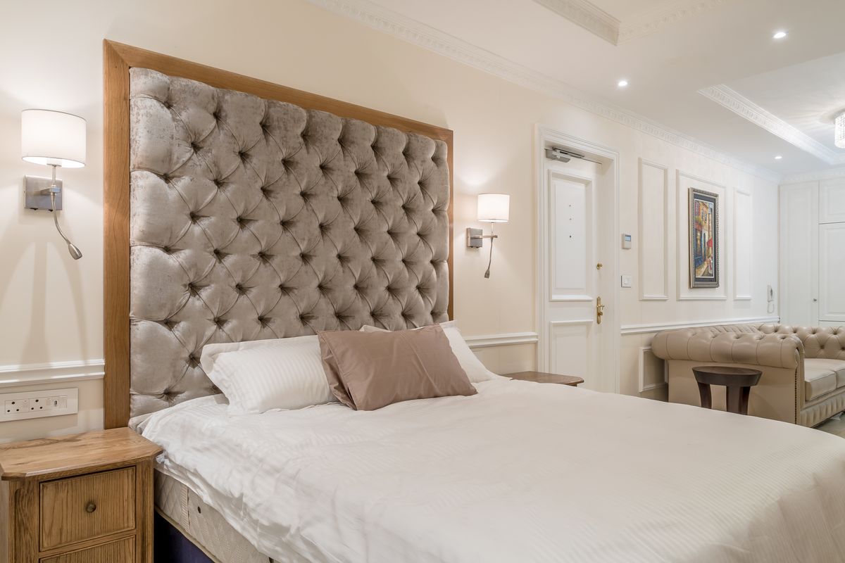 A well-appointed bedroom featuring elegant wall paneling, crown molding, recessed lighting, and integrated wall-mounted fixtures in a neutral, sophisticated color palette.