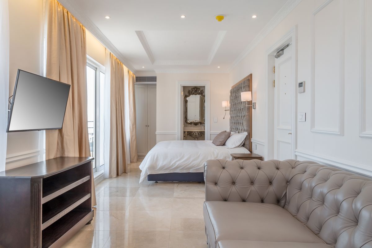 A well-appointed bedroom featuring marble flooring, crown molding, recessed lighting, and direct access to a balcony through sliding glass doors.