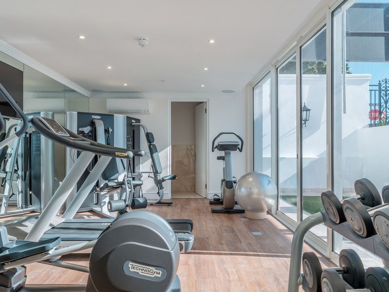A well-maintained private gym featuring mirrored walls, recessed lighting, split-system air conditioning, and large sliding glass doors providing natural light and outdoor access.