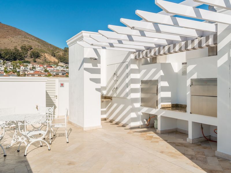 A spacious outdoor patio featuring a built-in braai area, granite countertops, a sink, and a white pergola, offering scenic mountain and neighborhood views.