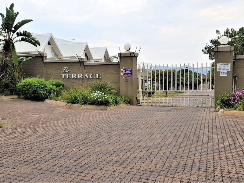 The entrance to The Terrace residential complex, featuring a secure gated access point, brick-paved driveway, and perimeter wall with electric fencing.