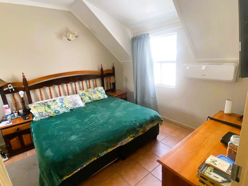 A cozy bedroom featuring tiled flooring, a sloped ceiling, and a wall-mounted air conditioning unit.