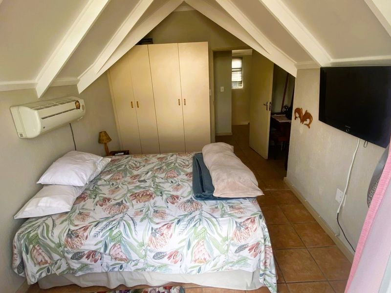 A cozy attic-style bedroom featuring a vaulted ceiling, built-in wardrobe, tiled flooring, and a wall-mounted air conditioning unit.