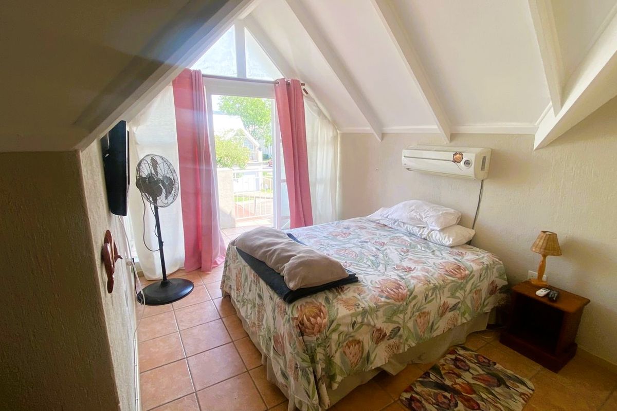 A cozy bedroom featuring a vaulted ceiling with exposed rafters, tiled flooring, and direct access to a balcony through a glass door.