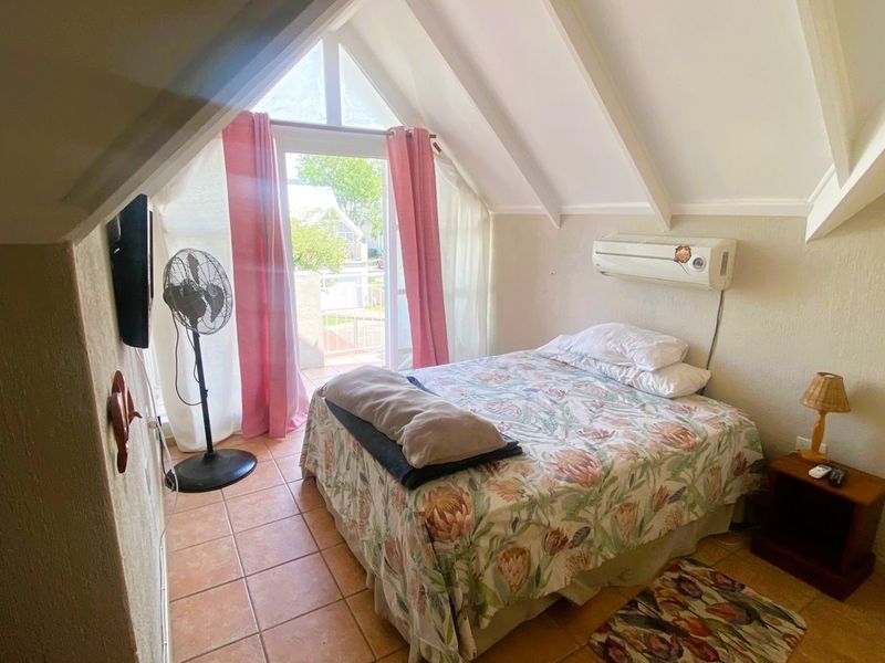 A cozy bedroom featuring a vaulted ceiling with exposed rafters, tiled flooring, and direct access to a balcony through a glass door.
