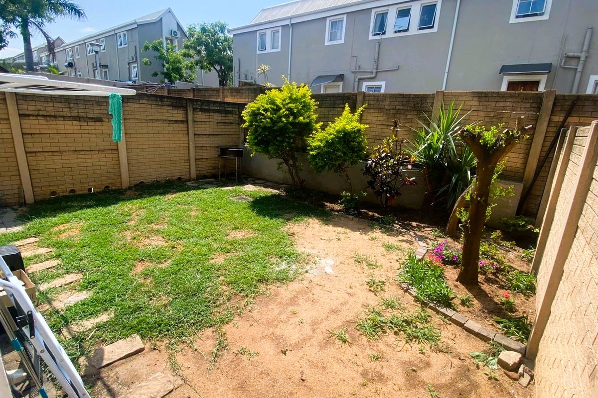 A private rear garden featuring a brick boundary wall, established shrubs, and a lawn area with paved stepping stones.