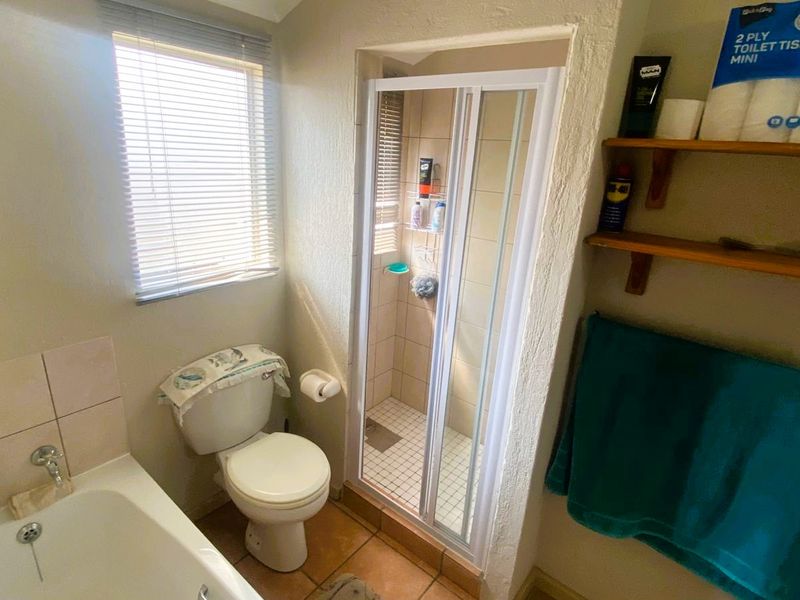 A functional bathroom featuring a bathtub, separate shower enclosure, and toilet, with tiled flooring and wall-mounted storage shelving.