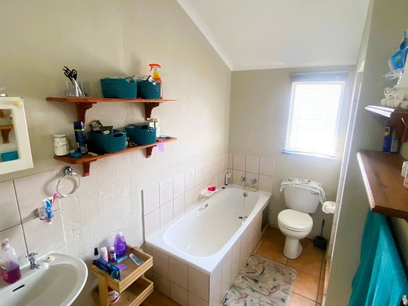 A functional bathroom featuring a built-in bathtub, pedestal washbasin, toilet, and tiled finishes, offering a practical layout with natural light from the window.