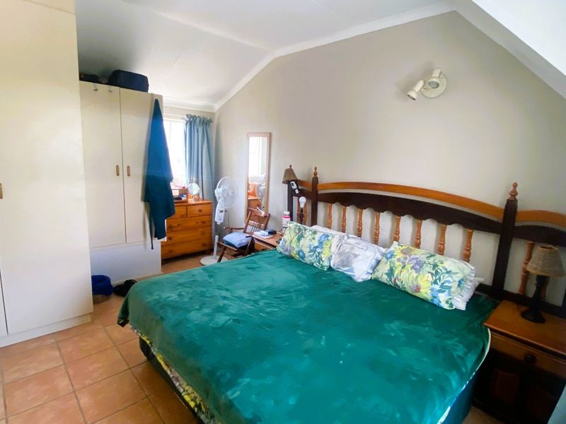 A bedroom featuring tiled flooring, built-in cupboards, and a sloped ceiling, providing a functional space with potential for modern updates.