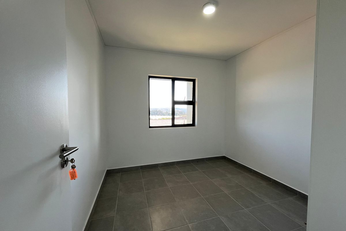 A clean, empty bedroom featuring neutral tiled flooring, white walls, and an aluminium-framed window providing natural light.