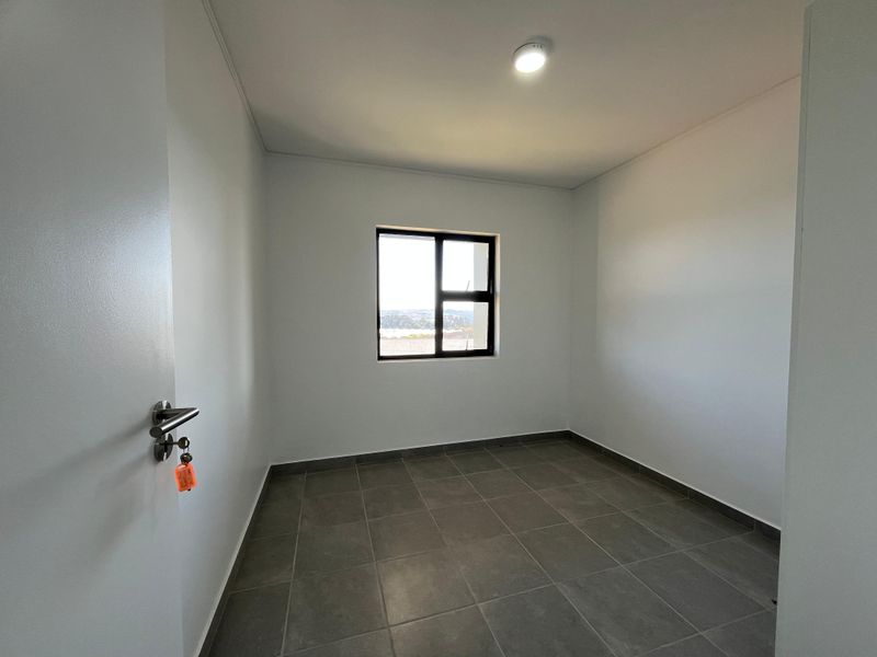 A clean, empty bedroom featuring neutral tiled flooring, white walls, and an aluminium-framed window providing natural light.