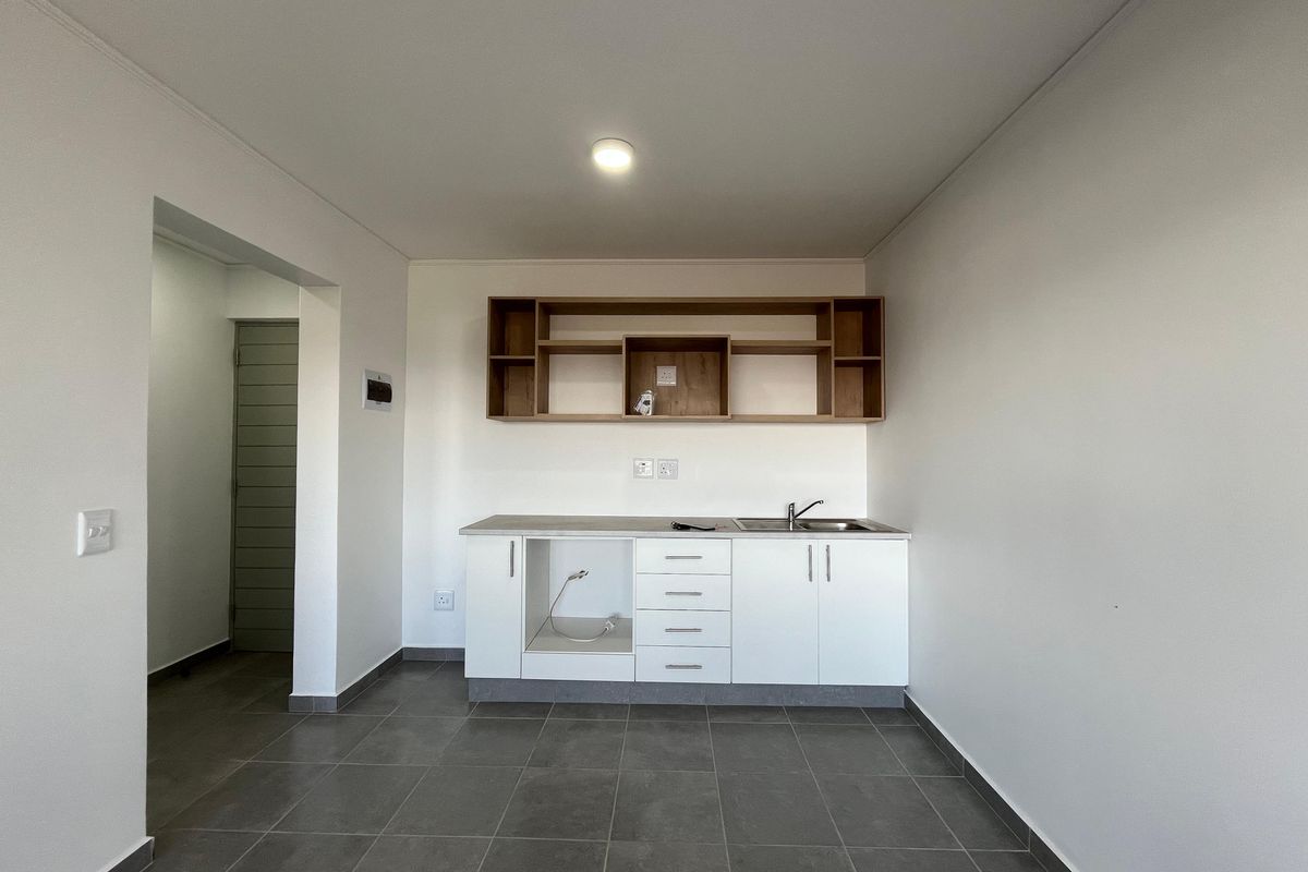 A clean, modern kitchen area featuring white cabinetry, open shelving, a stainless steel sink, and neutral tiled flooring in an open-plan layout.