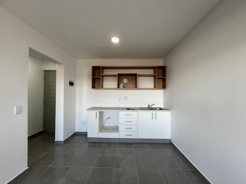 A clean, modern kitchen area featuring white cabinetry, open shelving, a stainless steel sink, and neutral tiled flooring in an open-plan layout.