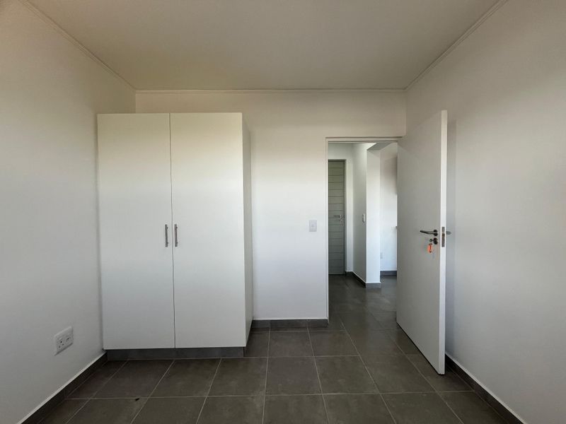 A clean, empty bedroom featuring neutral tiled flooring and a built-in white wardrobe, offering a blank canvas for personalization.