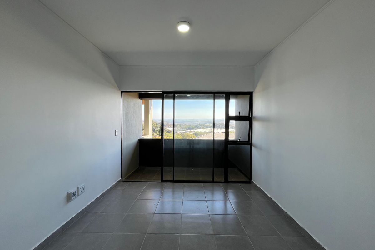 An empty, well-lit living area featuring neutral tiled flooring and a large sliding glass door that opens onto a balcony with scenic views.