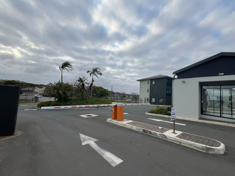 The property entrance features a secure boom gate access point with paved traffic islands and modern apartment building architecture.