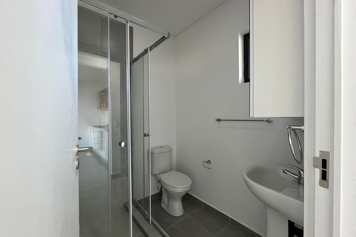 A clean and functional bathroom featuring a pedestal washbasin, a glass-enclosed shower, and a toilet, finished with neutral floor tiles.