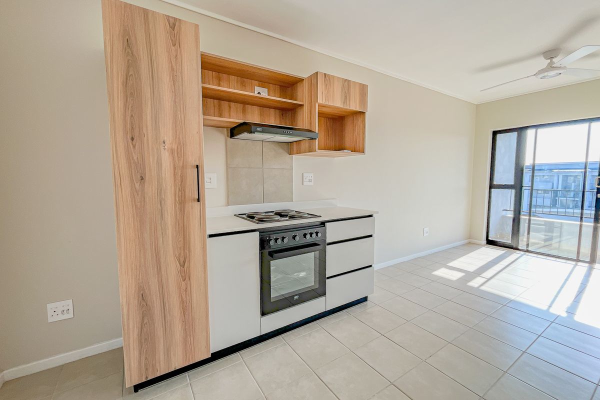 Modern kitchen featuring built-in cabinetry, oven, hob, and extractor fan, with tiled flooring and access to a balcony through a sliding glass door.
